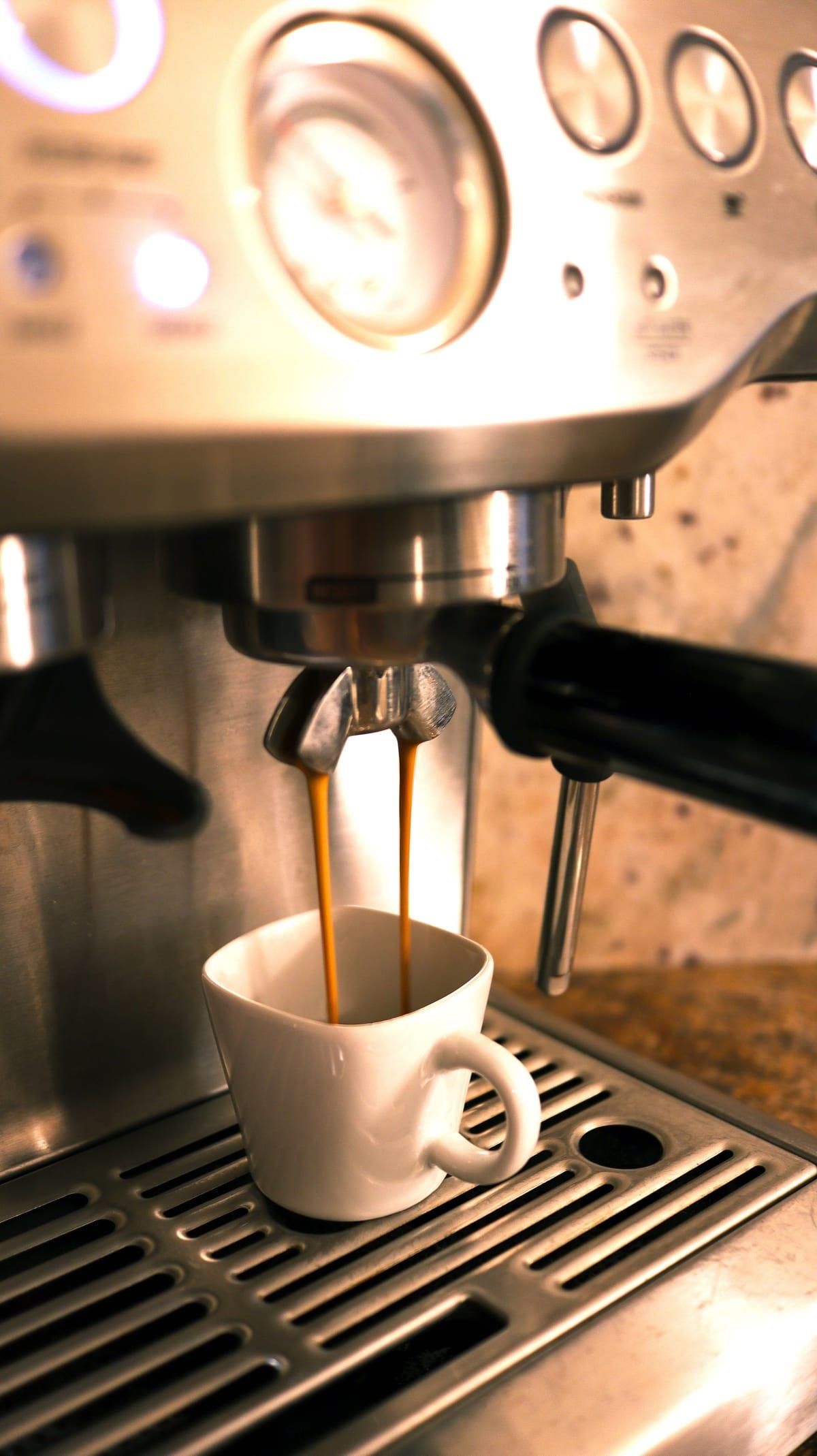 Un double espresso coulant d’une machine dans une petite tasse blanche, deux filets sombres tombant du porte-filtre